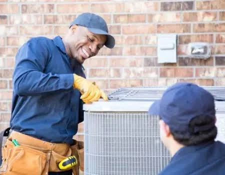 Two technicians inspecting the top of an outdoor air conditioner