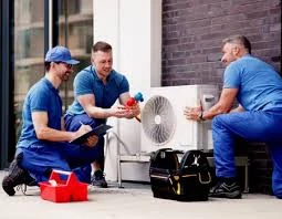 Three HVAC service professionals reviewing a compact outdoor air conditioning unit